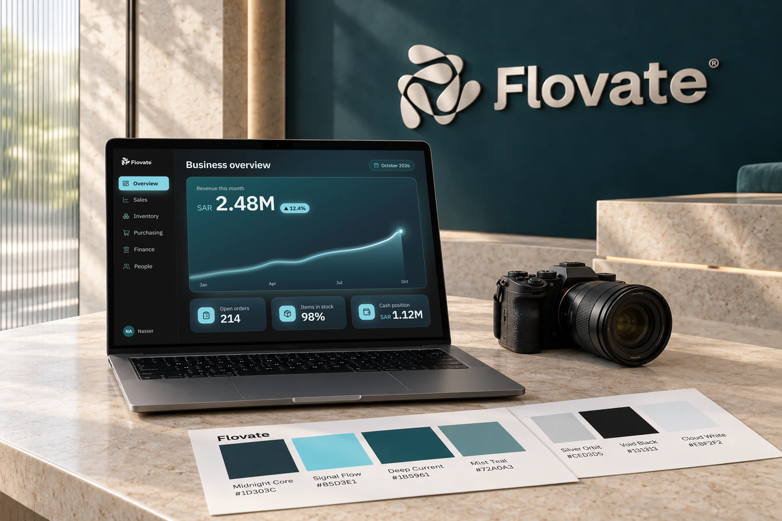 A laptop displaying the Flovate ERP dashboard beside a camera and brand color palettes in a refined teal-and-limestone office.